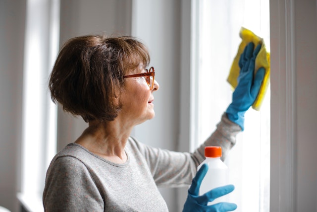 a middle aged cleaner with a bob haircut and brown glasses washes a window after a tenant moves out of a rental property